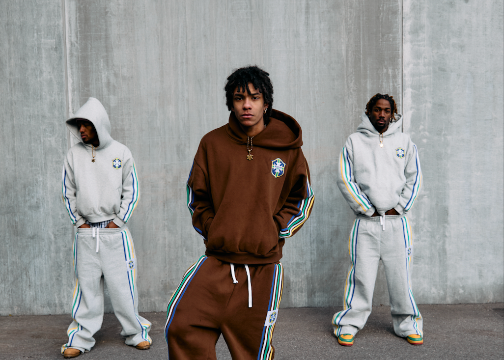 Three individuals wearing tracksuits standing against a concrete wall.